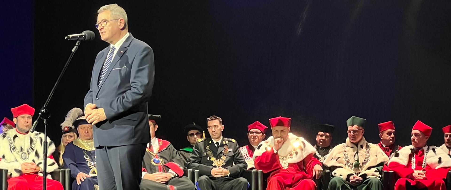 Wiceminister Wojciech Murdzek w Collegium Humanum, wiceminister Wojciech Murdzek stoi przed mikrofonem i przemawia, za nim siedzą władze uczelni.