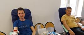 Na zajęciu widoczni dwaj mężczyźni jeden w granatowej koszulce i czarnych spodniach drugi strażak w koszulce i spodniach koloru piaskowego siedzący na krzesłach na sali podczas rejestracji i badania przed oddaniem krwi podczas akcji zbiórki krwi zorganizowanej przez Klub Honorowych Dawców Krwi Polskiego Czerwonego Krzyża przy Komendzie Powiatowej Państwowej Straży Pożarnej w Gorlicach