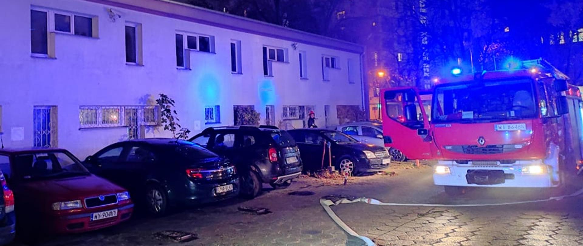 Na zdjęciu widoczny jest budynek w którym miał miejsce pożar, pracujący strażacy oraz samochód straży