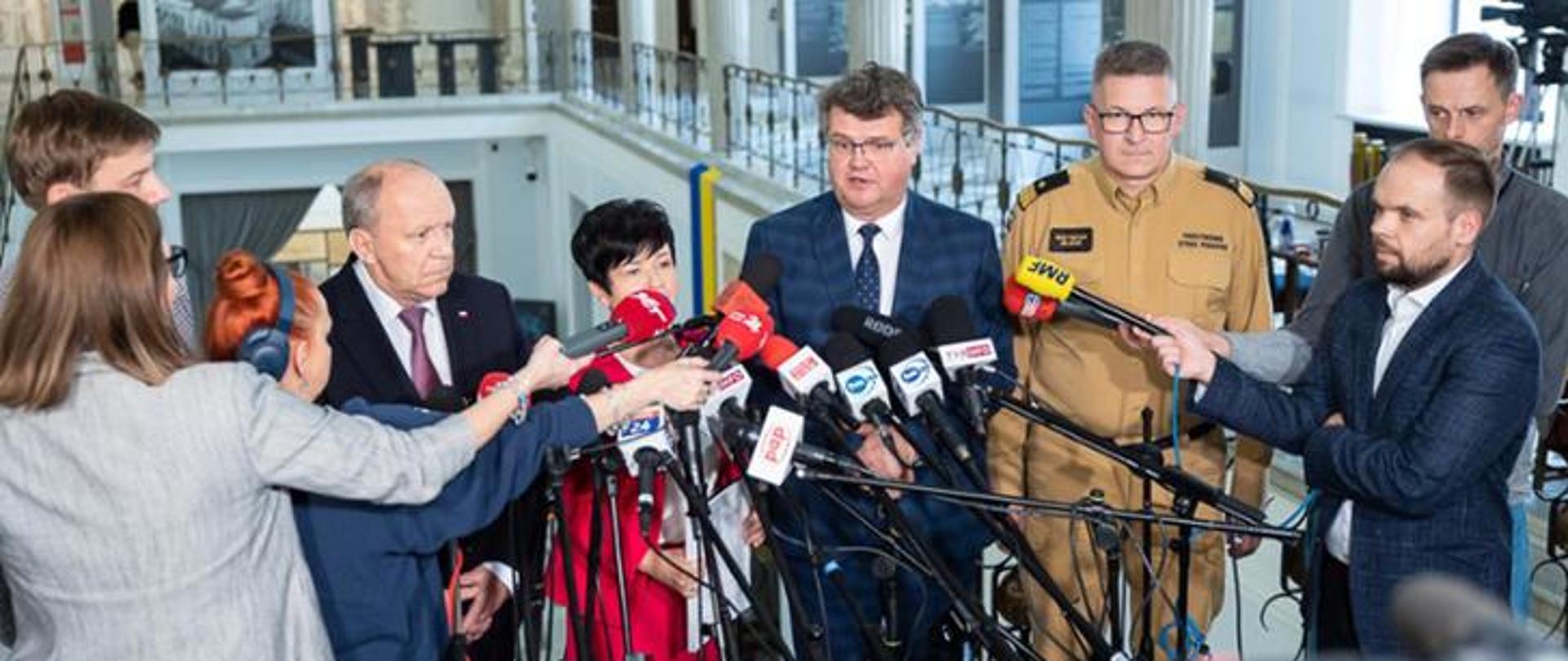 Zdjęcie przedstawia wiceministra Macieja Wąsika podczas udzielania wywiadu do mediów, związany z dotacją dla Młodzieżowych Drużyn Pożarniczych.