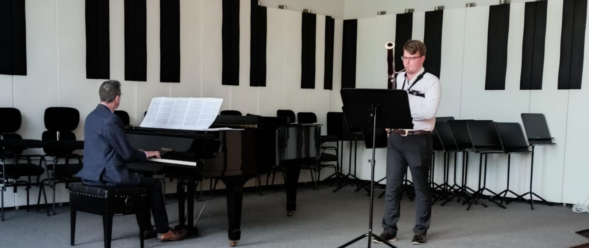 Chłopak gra na fagocie, mężczyzna akompaniuje na fortepianie.