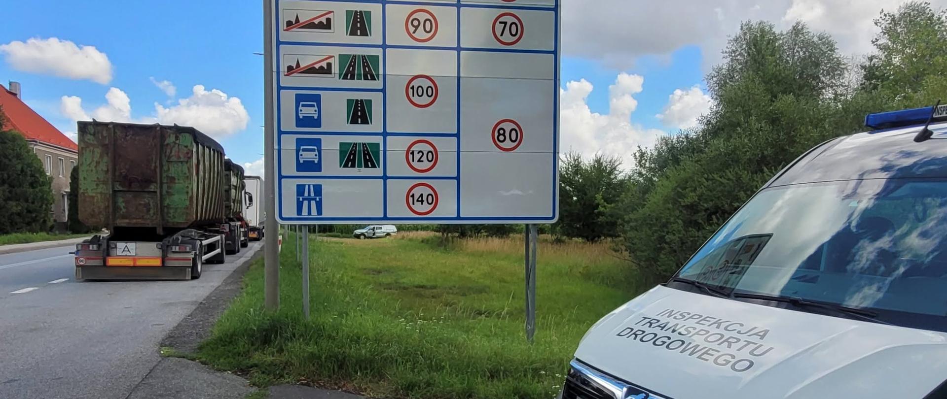 Pojazd Inspekcji Transportu Drogowego stoi przy drodze obok tablicy informacyjnej z ograniczeniami prędkości w Polsce. W tle widoczne są samochody ciężarowe oczekujące na kontrolę.