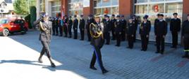 Zdjęcie przedstawia przegląd pododdziału. Nadbrygadier Andrzej Babiec Podkarpacki Komendant Wojewódzki Państwowej Straży Pożarnej w umundurowaniu galowym krokiem defiladowym oddając honor poprze salutowanie dokonuje przegląd pododdziału. Na zdjęciu w połowie pododdziału. Z nim po lewej stronie w odległości jednego kroku dowódca uroczystości w umundurowaniu galowym kapitan Marcin Bieszczad. Dowódca uroczystości oddaje honor poprzez salutowanie. W tle po lewej stronie nowy samochód operacyjny HONDA CRV. Obok samochodu w stoi strażak w umundurowaniu koszarowym. Dalej w prawo funkcjonariusze Komendy Powiatowej Państwowej Straży Pożarnej w Strzyżowie ustawieni w dwuszeregu. Z nimi widoczne bramy wyjazdowe garażów jednostki ratowniczo gaśniczej. Na początku pododdziału widoczne poczty flagowy i sztandarowy.