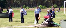 Zdjęcie przedstawia strażaka obsługującego motopompę wraz z sędziami zawodów