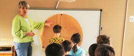 dzieci przyklejają pokolorowane ikonki z produktami żywnościowymi do dużego papierowego koła
