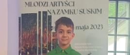 Twarz chłopca na tle baneru "Młodzi artyści na zamku Suskim".