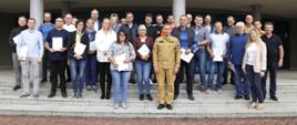 Grupowe zdjęcie uczestników szkolenia (26 osób) w towarzystwie Zastępcy Komendanta Centralnej Szkoły PSP, dwóch funkcjonariuszy CS PSP oraz kobiety