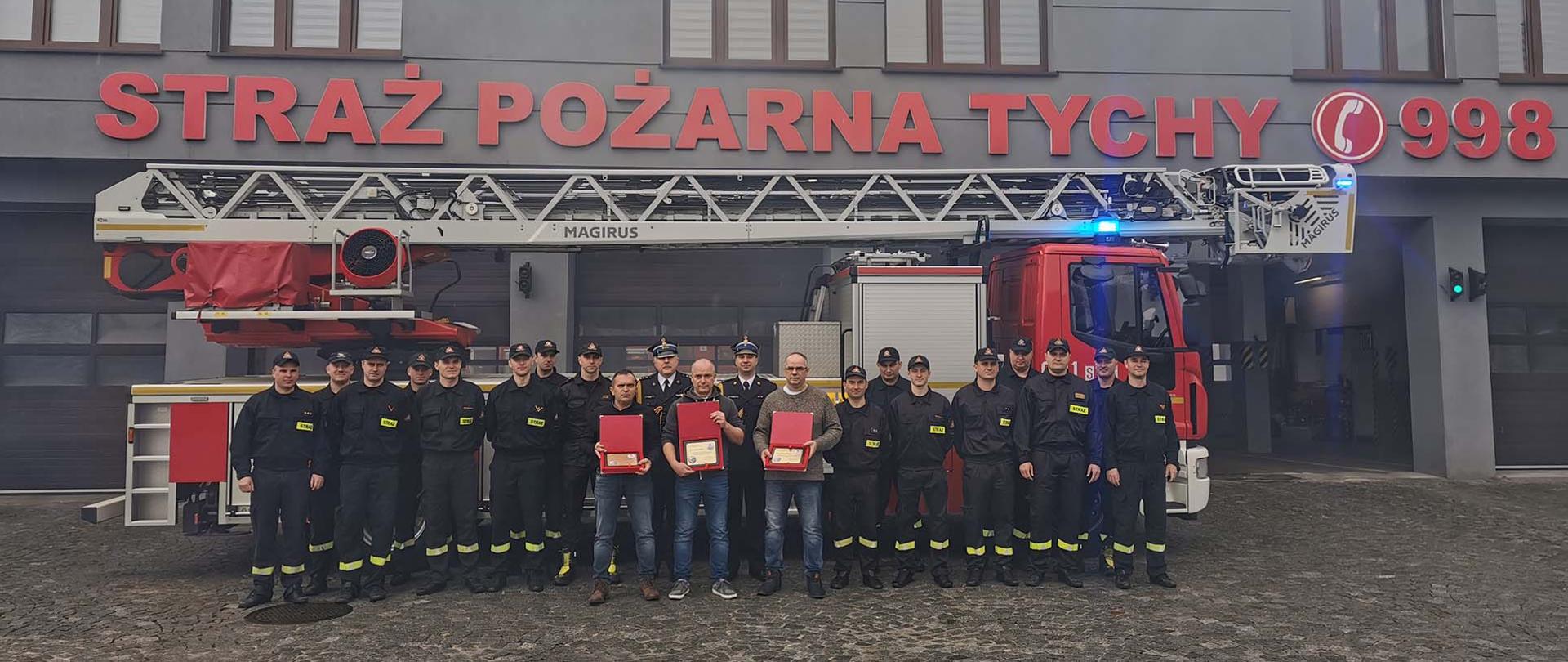 
Zbiórka strażaków wraz z Komendantem Miejskim i Dowódcą Jednostki Ratowniczo Gaśniczej na tle samochodu straży pożarnej