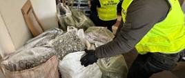 Osoby w kamizelkach służbowych stoją obok dużych worków wypełnionych suszem roślinnym.