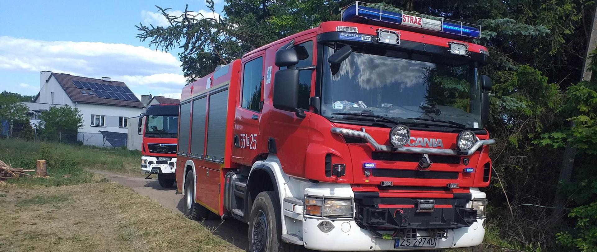 Zdjęcie przedstawia dwa wozy strażackie stojące na drodze gruntowej.