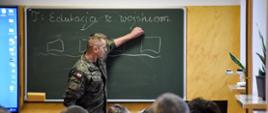 Żołnierz zapisuje na tablicy szkolnej temat lekcji: Edukacja z wojskiem