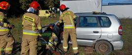 Strażacy w ubraniach specjalnych ćwiczą rozcinanie samochodu osobowego za pomocą specjalistycznego sprzętu.
