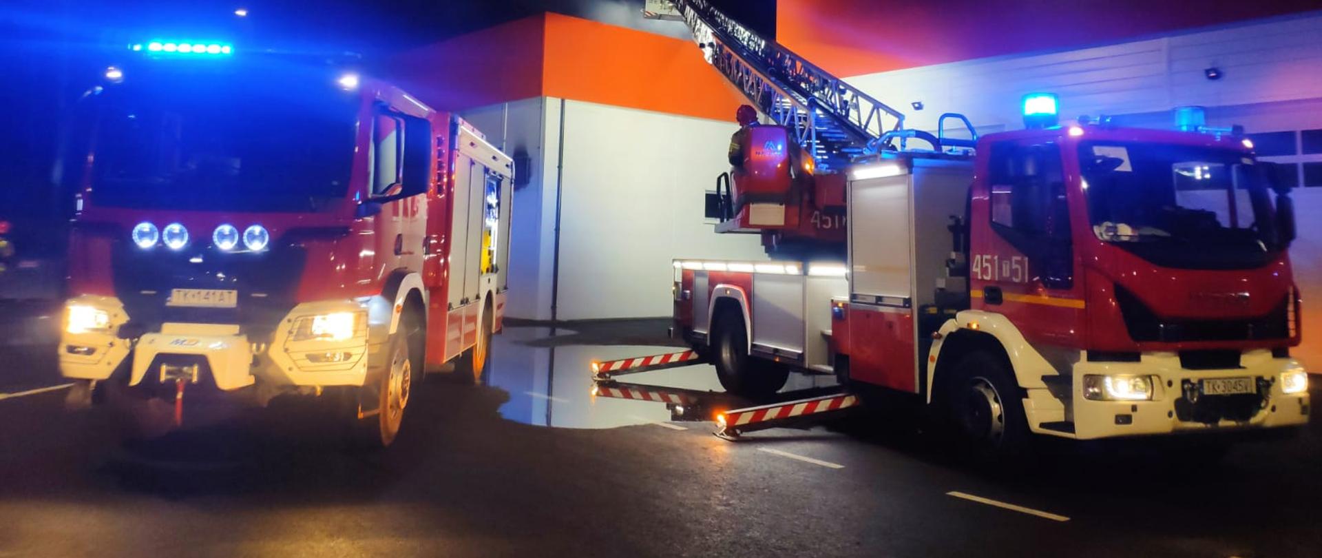 Strażacy w koszu drabiny mechanicznej gaszący pożar myjni . 