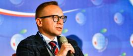 Wiceminister Artur Soboń przemawia do mikrofonu. W tle ścianka z logo Forum Ekonomicznego.