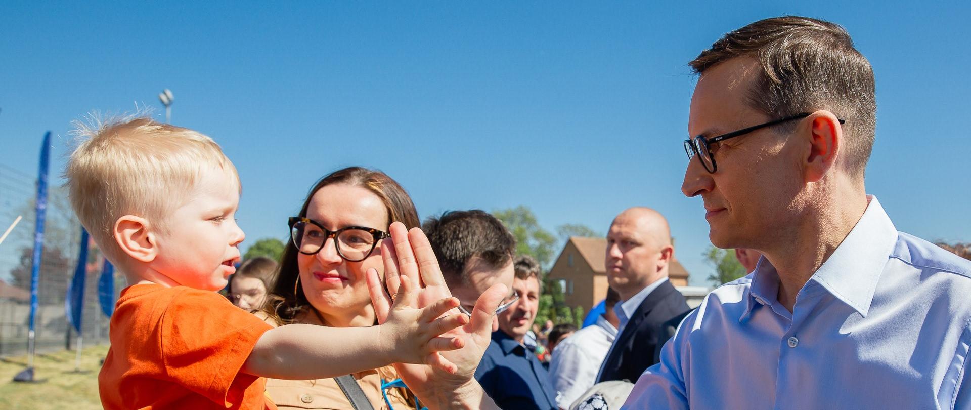 Premier Mateusz Morawiecki przybija piątkę z chłopcem na pikniku