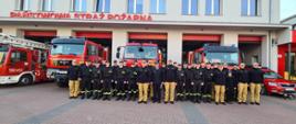 Widać strażaków na zdjęciu grupowym, za nimi samochody strażackie