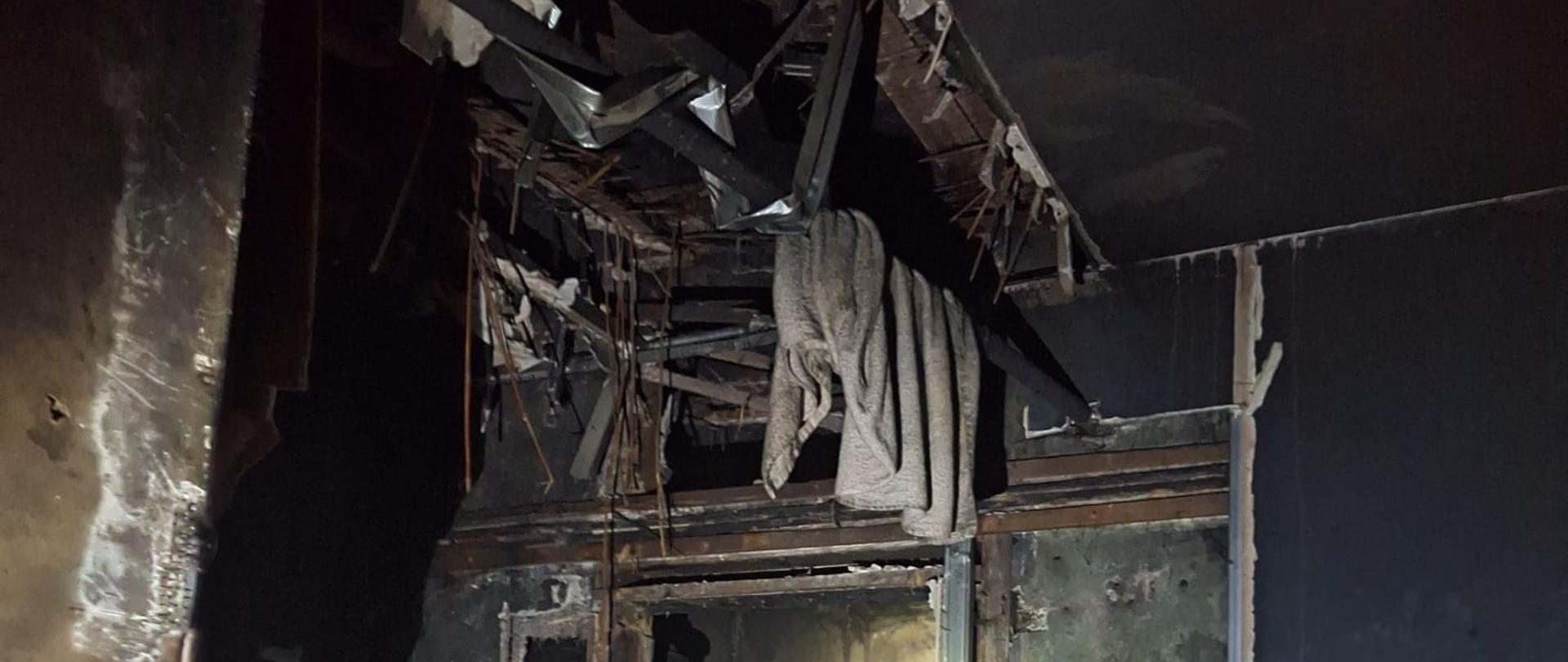 Skutki działania pożaru na tle zniszczonego mieszkania.