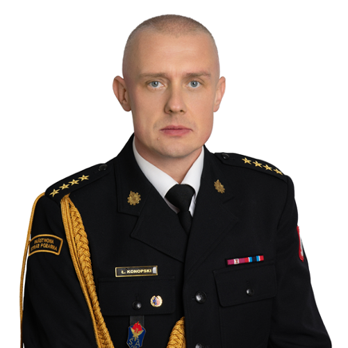 Zdjęcie przedstawia Łukasz Konopskiego, Zastępcę Komendanta Powiatowego Państwowej Straży Pożarnej w Zwoleniu. Jest to portret mężczyzny w mundurze galowym strażaka, z widocznymi dystynkcjami na pagonach. Na piersi munduru widoczne są baretki odznaczeń