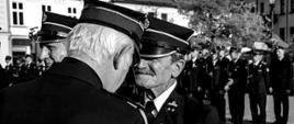 Widok z przodu. Druh Andrzej odznaczany odznaką św. Floriana przez kapelana małopolskich strażaków. W tle pododdział funkcjonariuszy Państwowej Straży Pożarnej. 