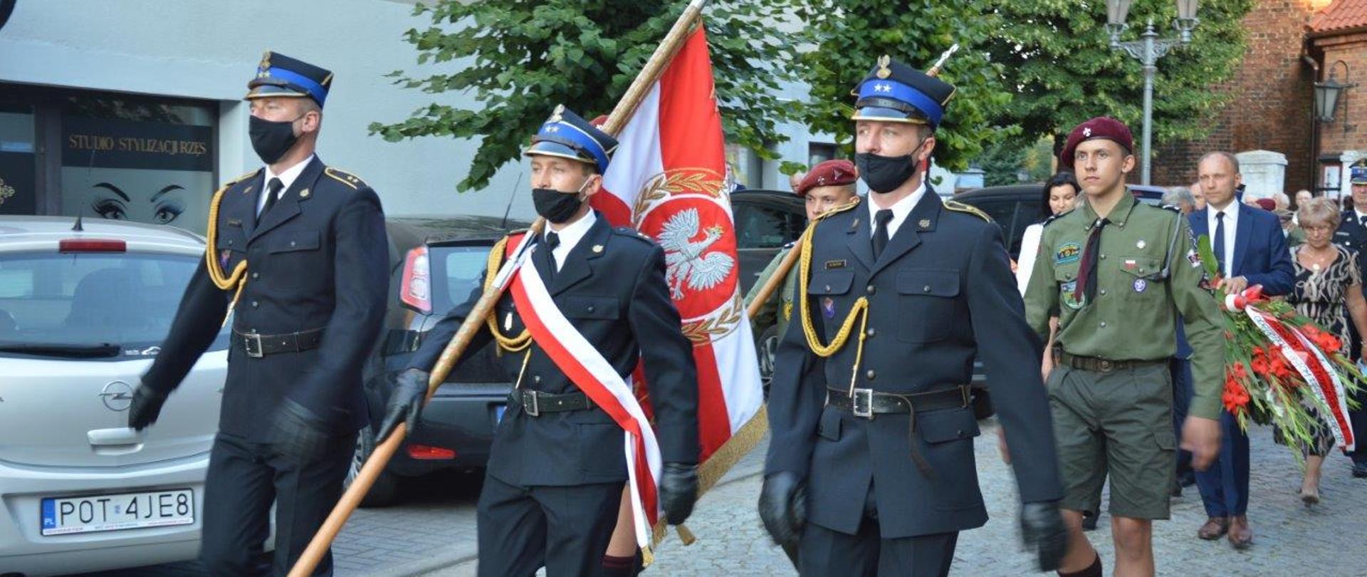 Zdjęcie przedstawia uroczystości związane z corocznym Świętem Wojska Polskiego w Ostrzeszowie. Na zdjęciu widać poczet sztandarowy biorący udział w uroczystościach. Zdjęcie wykonane w porze dziennej na ostrzeszowskim rynku.