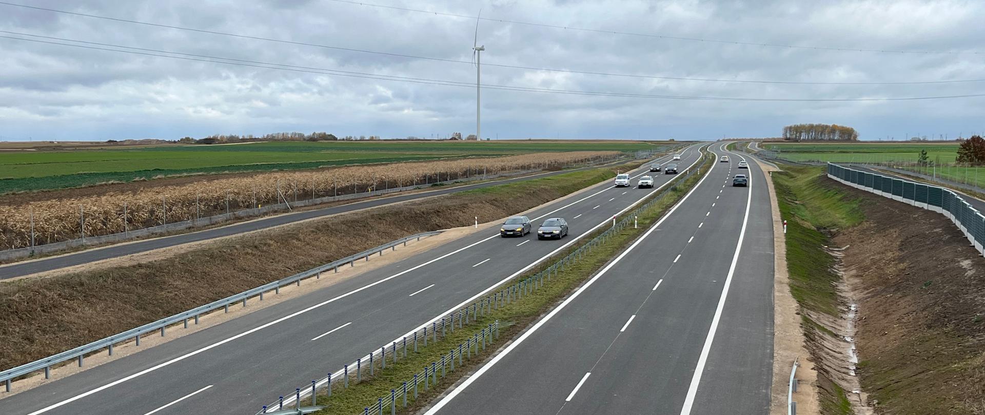 Widok z wiaduktu na biegnącą dołem, dwujezdniową drogę z pasem rozdziału w środku. W środkowej części zdjęcia nadjeżdżające samochody osobowe