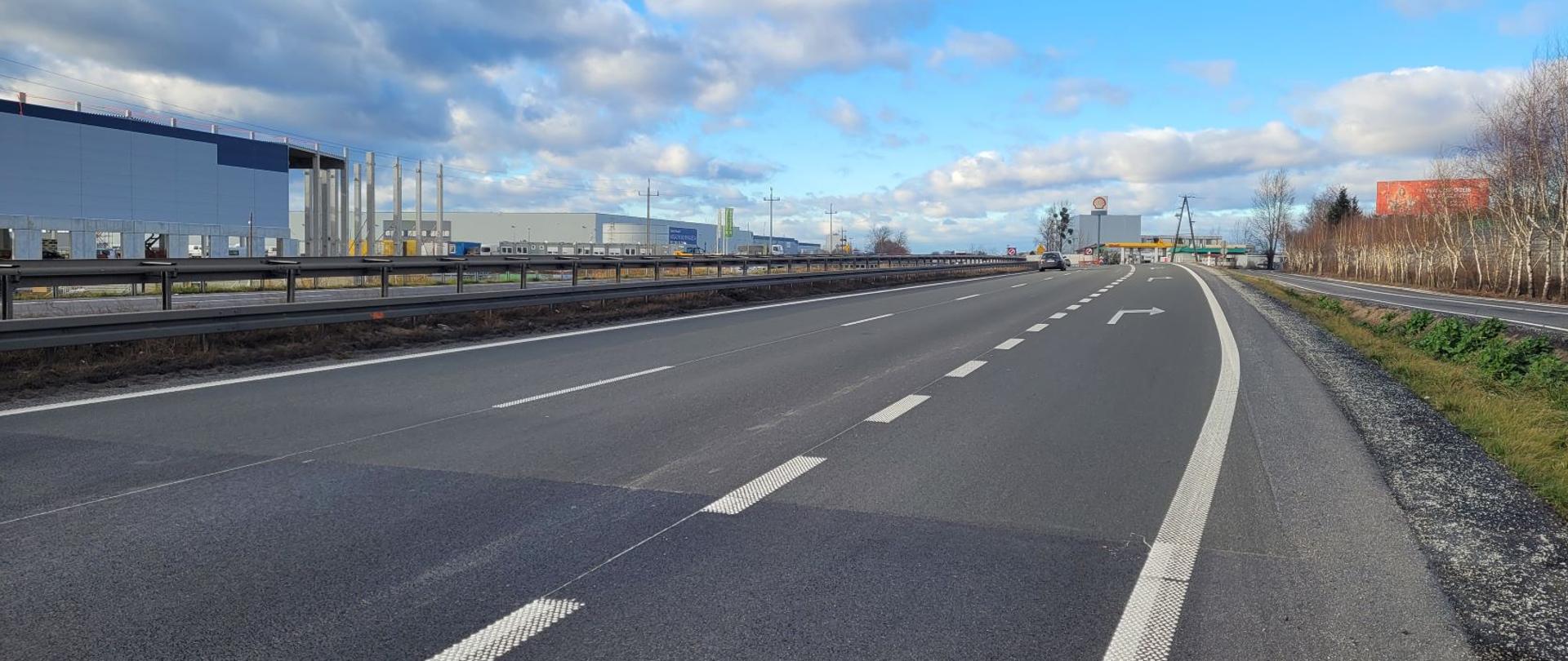 Droga ekspresowa dwujezdniowa, w tle zabudowania przemysłowe.