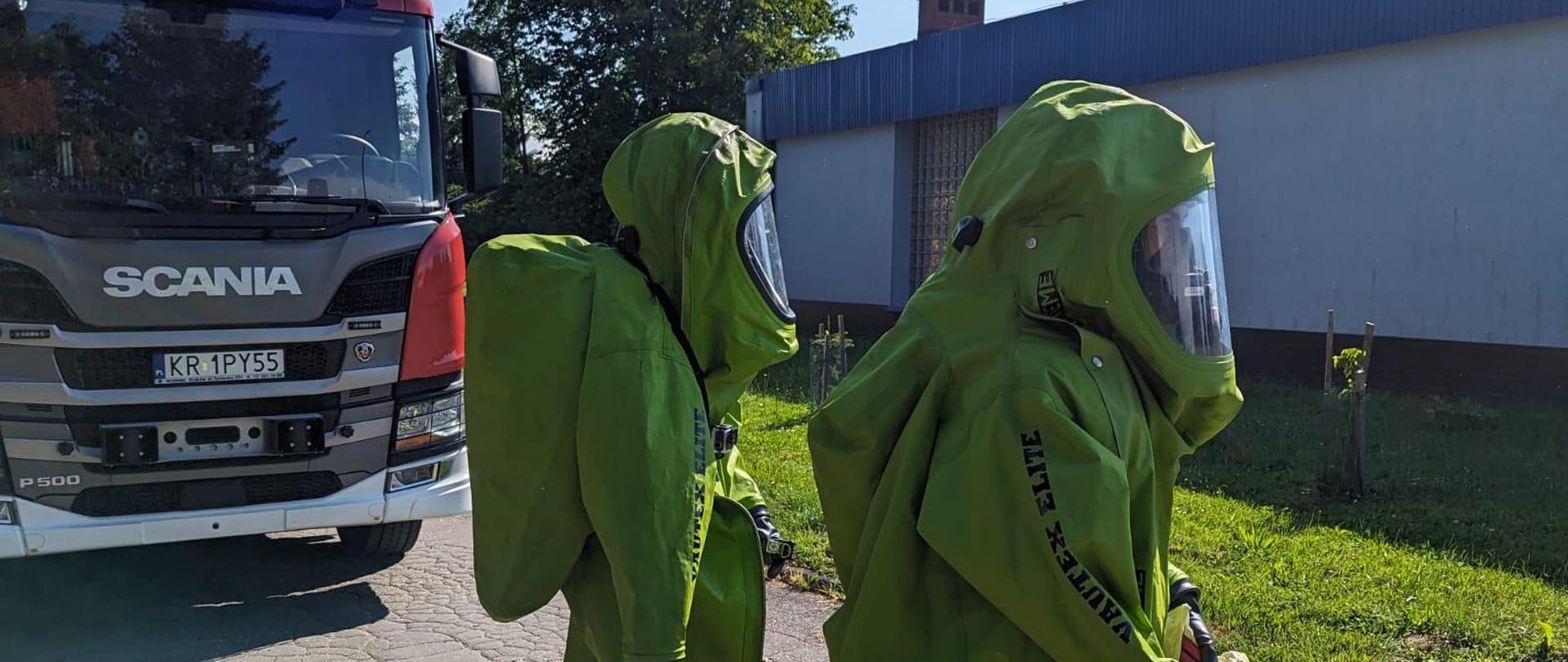 Strażacy w ubraniach gazoszczelnych przed budynkiem