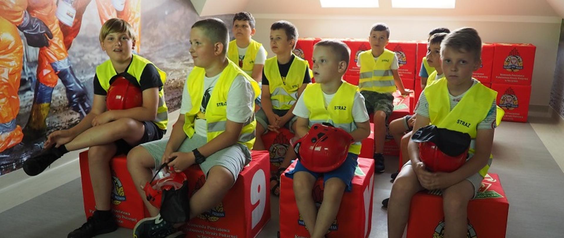 Zdjęcie przedstawia dzieci siedzące na pufach w sali multimedialnej