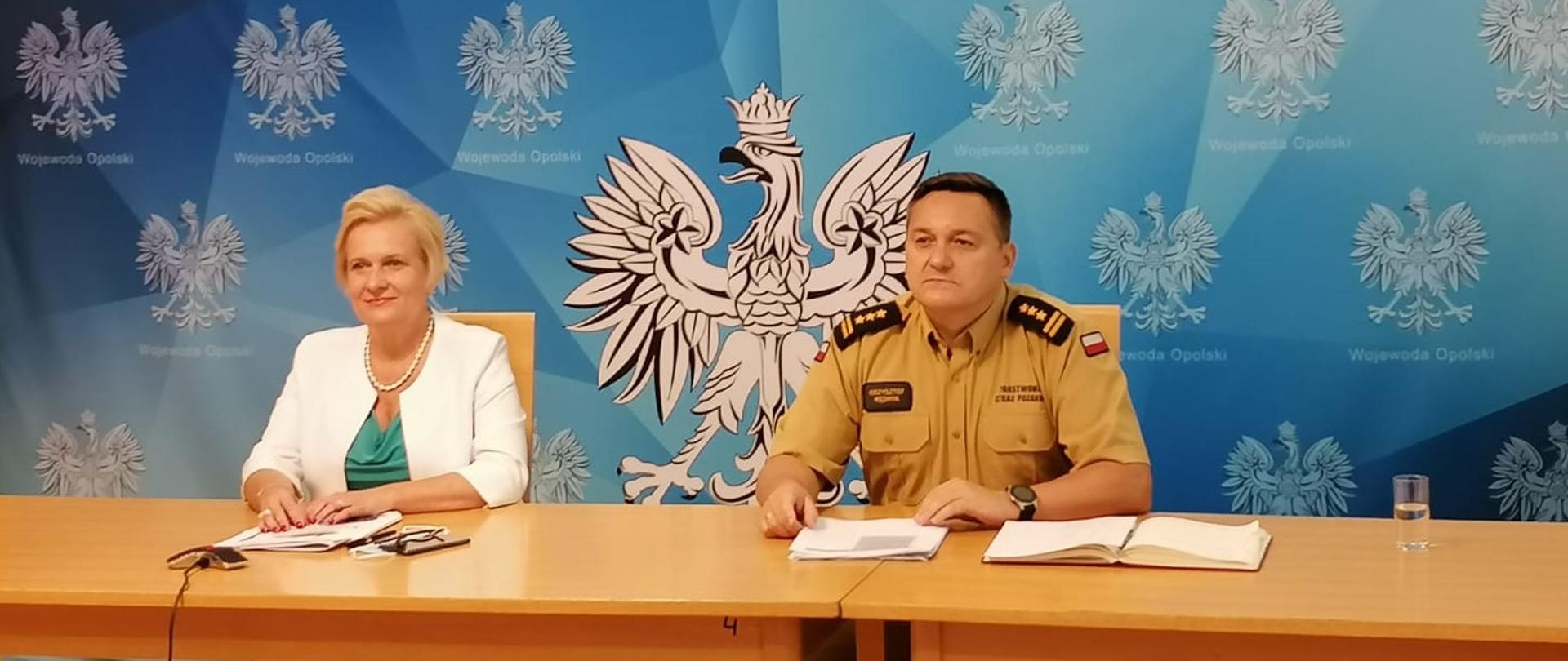 Zdjęcie przedstawia Wicewojewodę Opolskiego oraz Komendanta Wojewódzkiego PSP siedzących przy stole na tle niebieskiego baneru z napisem "Wojewoda Opolski".