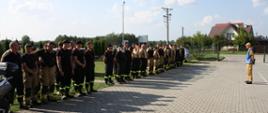 Zbiórka strażaków OSP przed rozpoczęciem ćwiczeń. Po lewej stronie w dwuszeregu stoją strażacy OSP, na przeciw nich stoi organizator ćwiczeń funkcjonariusz KP PSP w Starachowicach.