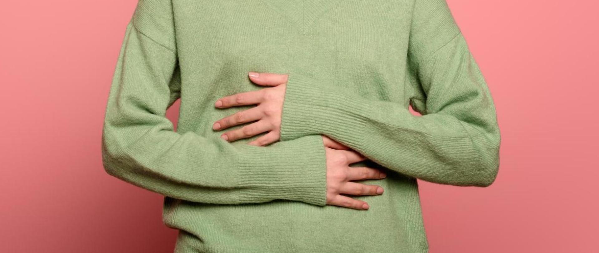 Na zdjęciu jest kobieta trzymająca ręce na brzuchu - na wysokości układu pokarmowego.