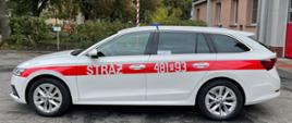 NOWY SAMOCHÓD W KOŚCIAŃSKIEJ KOMENDZIE. Na zdjęciu samochód Skoda Octavia, kolor biały, czerwony pas na wysokości klamek od drzwi z napisem straż i numer operacyjny, w tle budynek Komendy. 