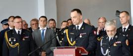 Przy mównicy Komendant PSP w Radomsku w umundurowaniu galowym w tle zgromadzeni goście.