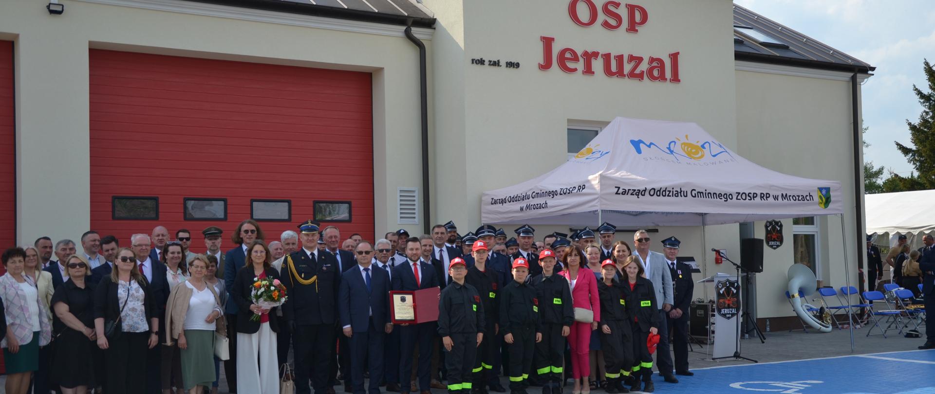 Zdjęcie grupowe uczestników uroczystości stojących na tle nowej remizy OSP Jeruzal. 