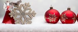 Na białym futrzanym nakryciu, od lewej strony ustawione ozdoby choinkowe: aniołek, drewniana ozdoba w kształcie łatka śniegu, oraz dwie czerwone bombki ze złotą aplikacją w kształcie płatków śniegu. 