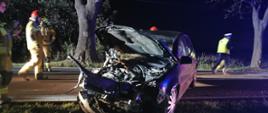 Na zdjęciu widać rozbite auto oraz strażaków i policjanta 