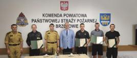Kolorowa fotografia wykonana w pomieszczeniu. Przedstawia grupę strażaków w strojach służbowych i cywilnych po wręczeniu listów gratulacyjnych przez starostę brzozowskiego i komendanta PSP w Brzozowie