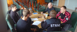 Na zdjęciu znajdują się strażacy siedzący przy stole