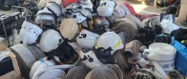 Zdjęcie przedstawia sprzęt strażacki: węże, buty, hełmy, urania znajdujące się na posadzce w garażu, które będą przekazane strażakom z Ukrainy, 