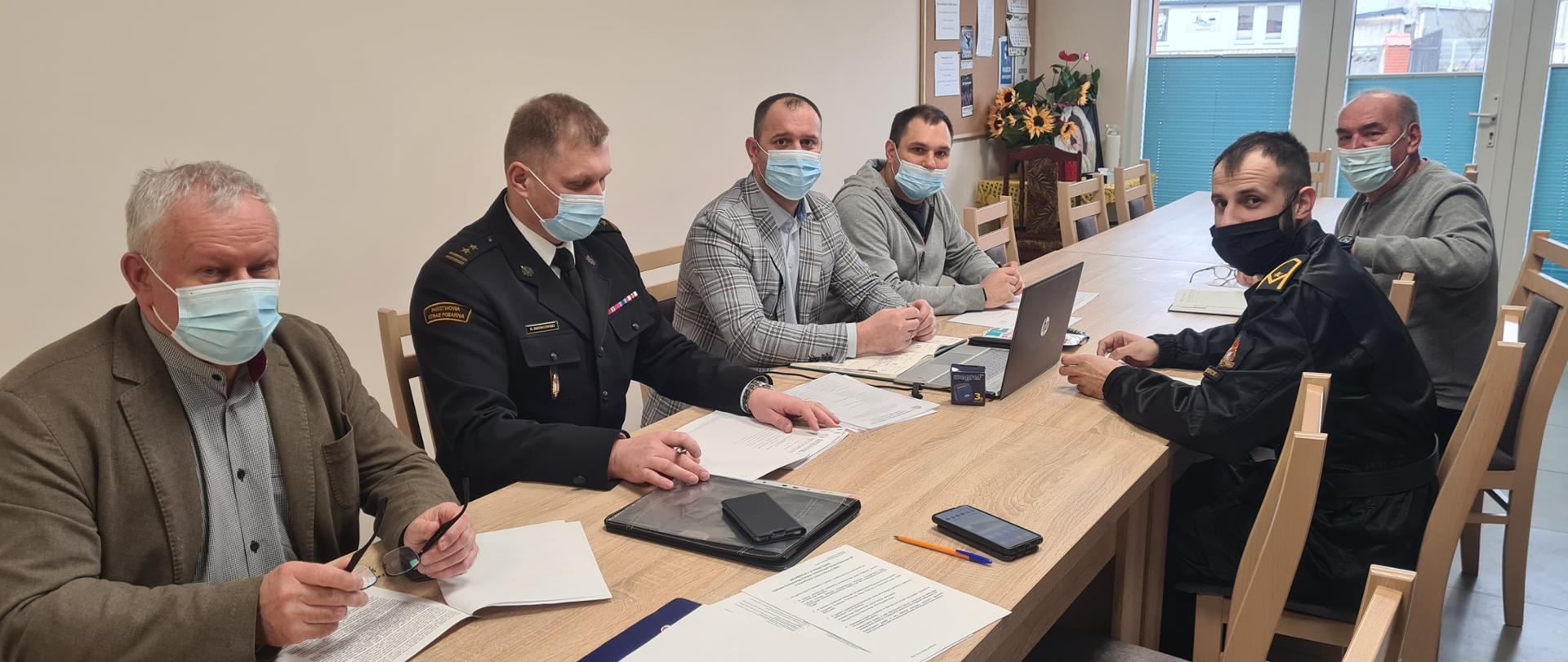 przy stole siedzą osoby wchodzące w skład Prezydium Zarządu Oddziału Powiatowego ZOSP RP w Kozienicach