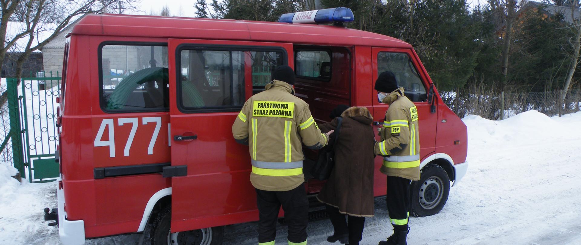 czerwony samochód pożarniczy dowozi osoby starsze na szczepienie