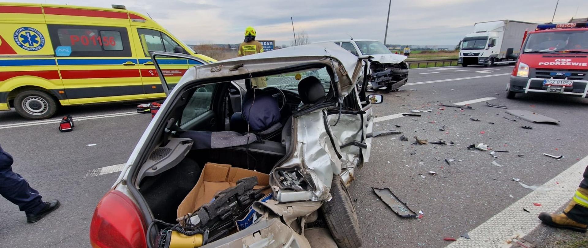 Widać mocno uszkodzony srebrny samochód od tyły, po lewej Karetka pogotowia, po prawej samochód strazacki