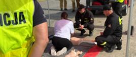 Zdjęcie przedstawia funkcjonariuszy Państwowej Straży Pożarnej oraz Policji uczących pierwszej pomocy.