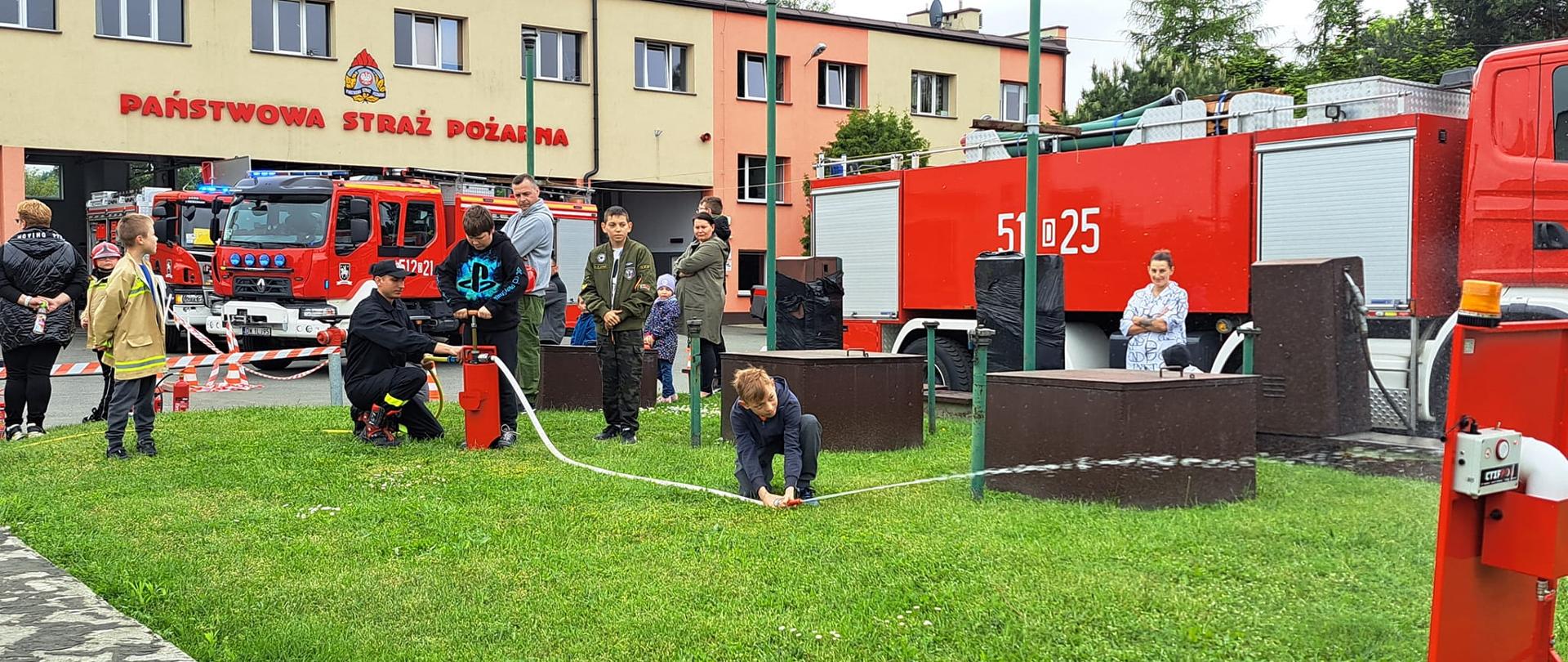 Na zdjęciu widać dzieci, które leją wodę do nalewaków z węży strażackich. 