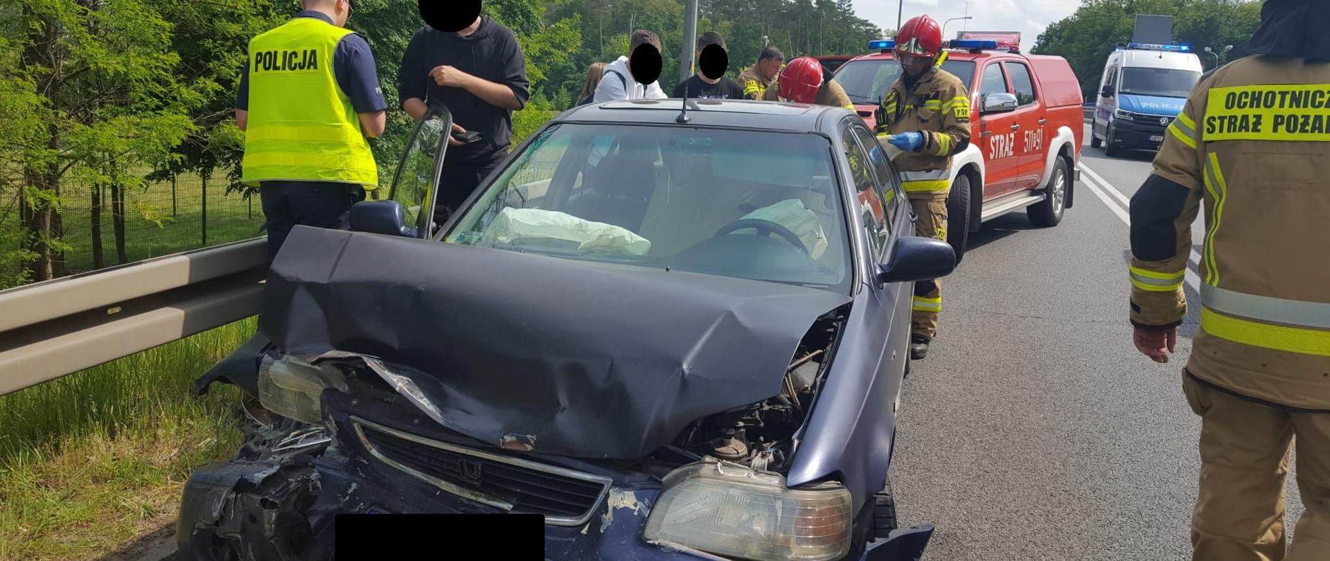 Strażacy i uczestnicy zdarzenia przy rozbitym pojeździe