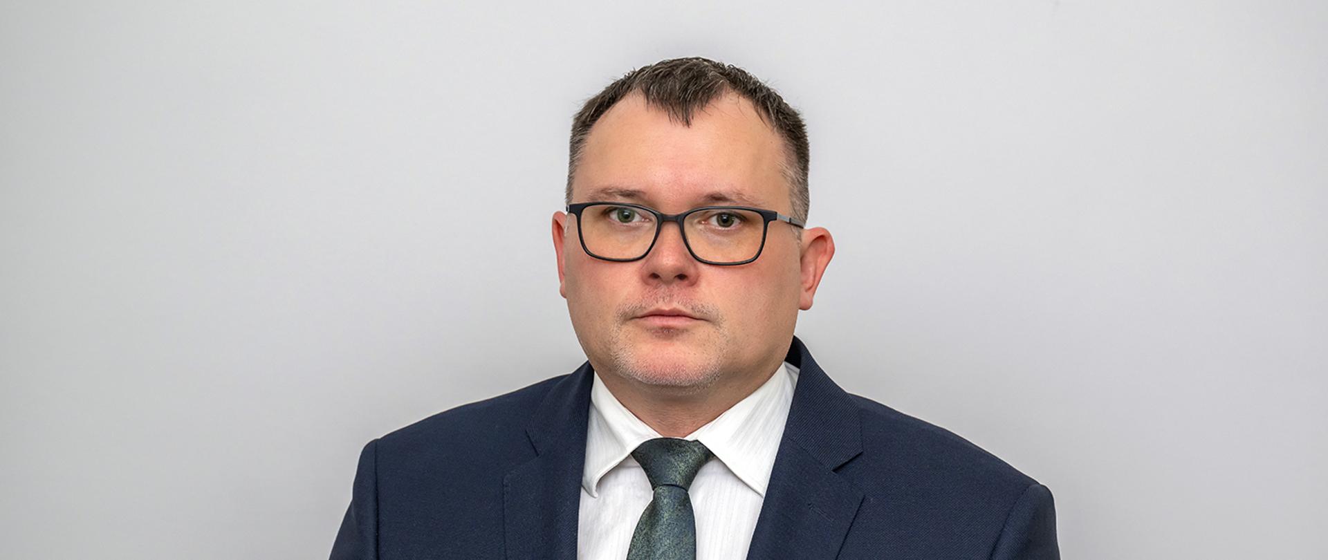 Członek Rady - Pan Paweł Szewczyk, na szarym tle elegancko ubrany w okularach