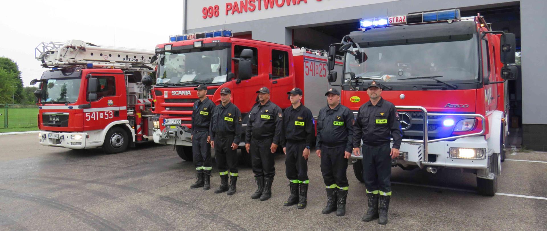 Strażacy stojący w szeregu przed budynkiem komendy.