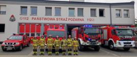Na zdjęciu widać strażaków na tle pojazdów pożarniczych i budynku komendy.