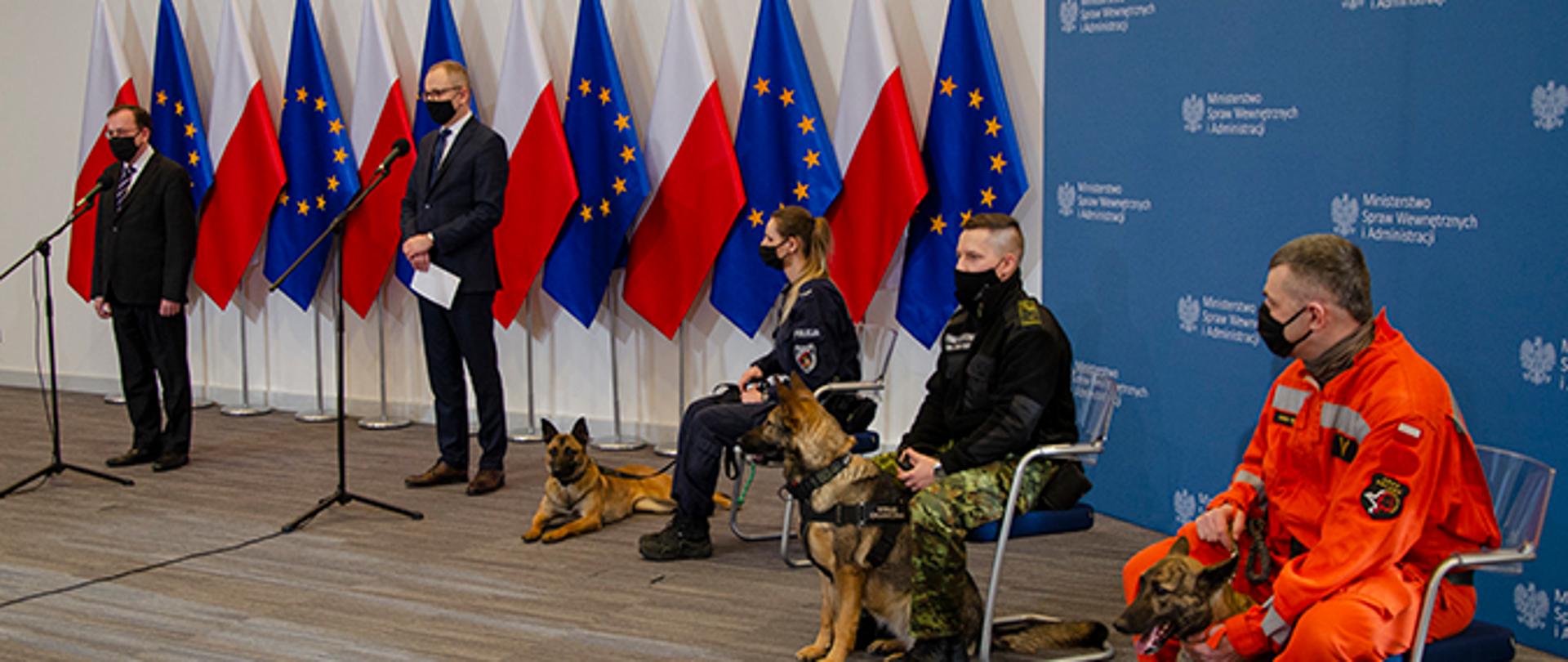 Na zdjęciu widoczna Aula w której odbywa się konferencja prasowa ministra MSWiA. Na stołkach siedzą przedstawiciele służb wraz ze swoimi psami.