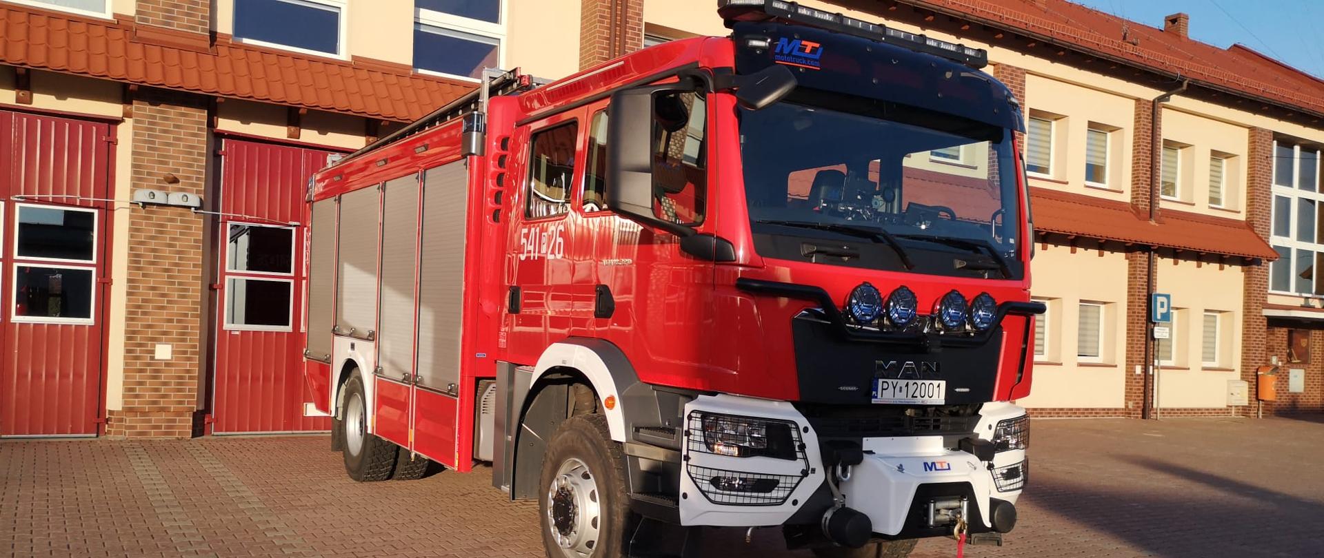 Na zdjęciu ciężki samochód gaśniczy marki MAN na placu manewrowym przed garażami Jednostki Ratowniczo-Gaśniczej